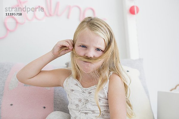 Porträt eines kleinen Mädchens  das mit seinen Haaren Schnurrbart macht.