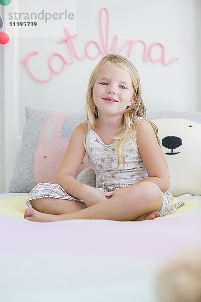 Porträt eines glücklichen kleinen Mädchens  das auf dem Bett sitzt