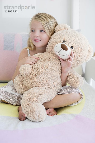 Glückliches kleines Mädchen mit Teddybär im Bett