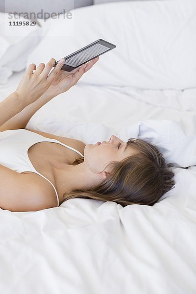 Frau auf dem Bett liegend mit einem digitalen Tablett