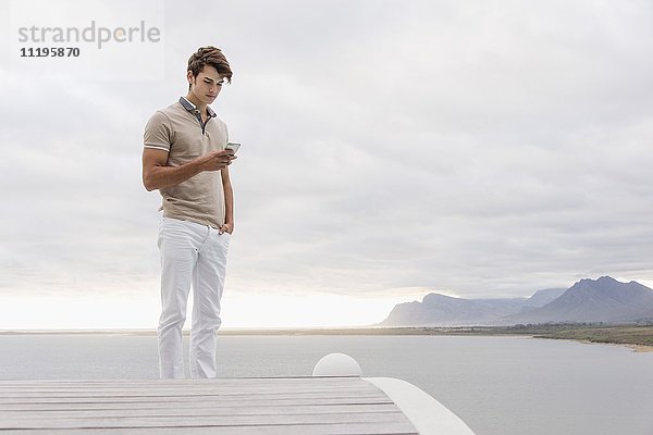 Junger Mann mit einem Smartphone am Seeufer