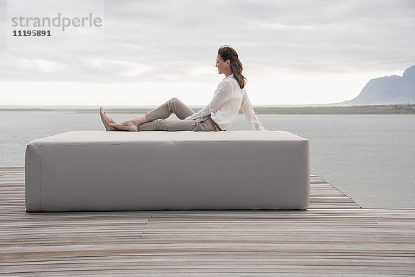 Seitenprofil einer reifen Frau  die auf einem Hocker am Seeufer sitzt