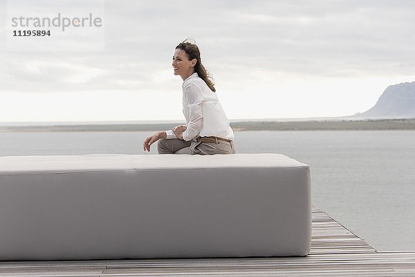 Fröhliche reife Frau sitzt auf einem Hocker am Seeufer