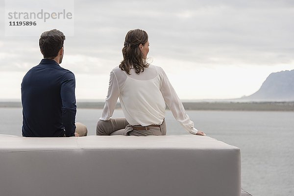 Reife Frau und mittelgroßer Mann auf einem Hocker sitzend mit Blick auf eine Aussicht