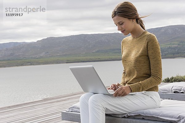 Glückliche junge Frau mit einem Laptop am Seeufer