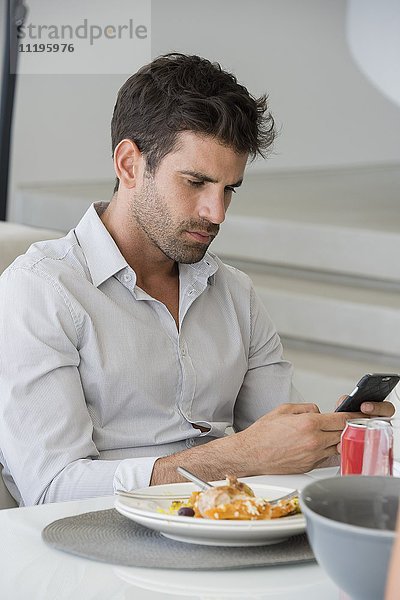 Mid Erwachsene Mann mit einem Smartphone am Esstisch