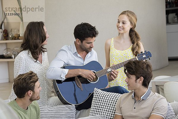 Glücklicher Mann  der mit seinen Freunden um ihn herum Gitarre spielt.