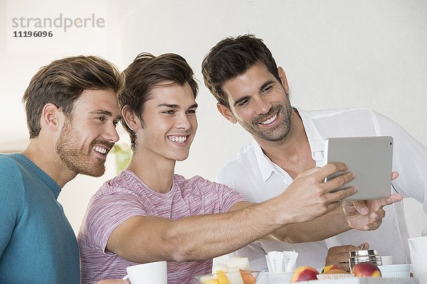 Glückliche männliche Freunde  die Selfie mit Tablette auf dem Frühstückstisch zu Hause einnehmen