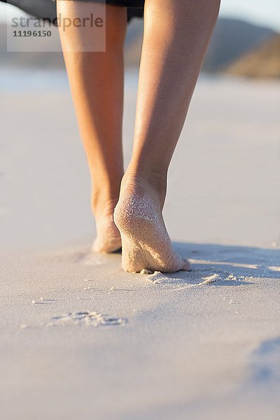 Blick auf eine Frau  die am Strand spazieren geht.