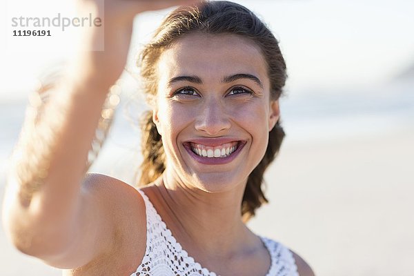 Glückliche junge Frau nimmt Selfie mit Smartphone am Strand