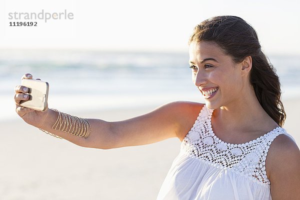 Schöne junge Frau  die Selfie mit Smartphone am Strand nimmt