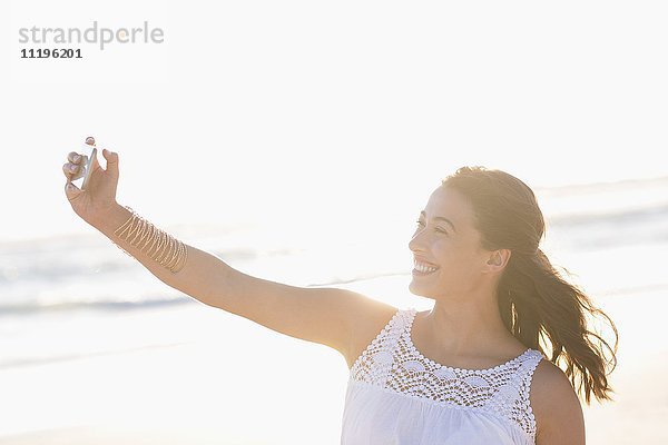 Schöne junge Frau  die Selfie mit Smartphone am Strand nimmt
