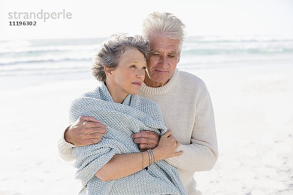 Alter Mann  der seine Frau von hinten am Strand umarmt.