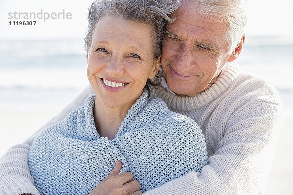 Alter Mann umarmt seine glückliche Frau von hinten am Strand.