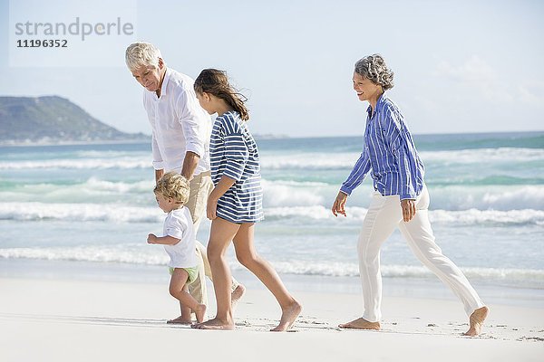 Altes Paar  das mit seinen Enkelkindern am Strand spazieren geht.