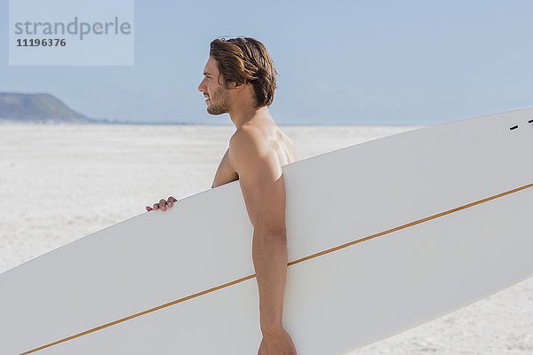 Seitenprofil eines Mannes mit Surfbrett am Strand
