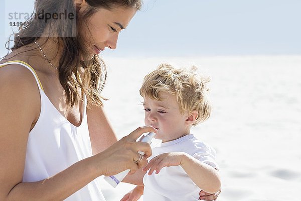 Frau spritzt Sonnencreme auf ihre Babyhand