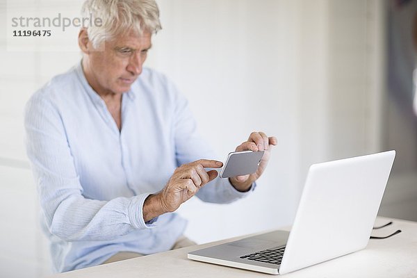 Senior Mann fotografiert Laptop-Bildschirm mit Kamera-Handy
