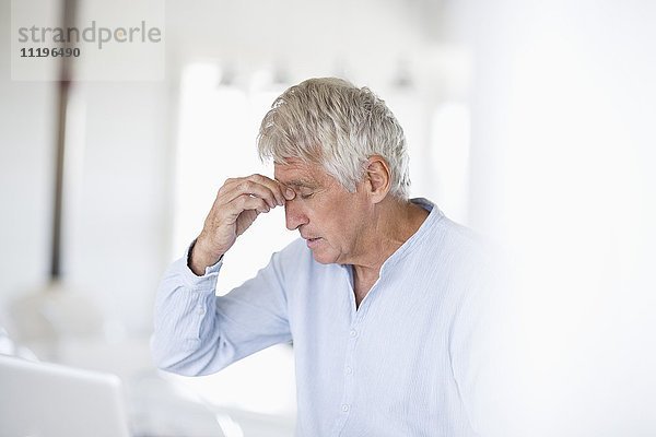 Besorgter älterer Mann Kopf in Hand mit Laptop auf dem Tisch