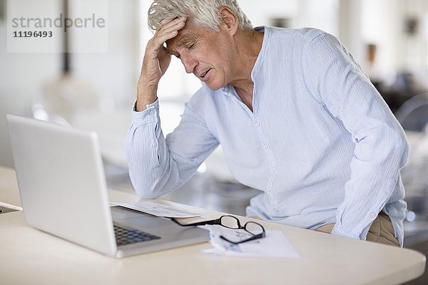 Besorgter älterer Mann mit Rechnungen und Laptop auf dem Tisch