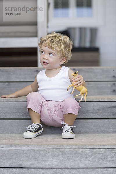 Süßer Junge sitzend auf einer Treppe mit Spielzeug