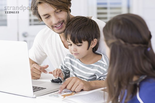 Vater lehrt die Kinder über die Weltkarte  während sie den Laptop zu Hause benutzen.