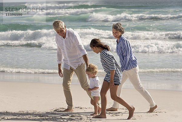 Glückliche Großeltern  die mit Enkelkindern am Strand spazieren gehen