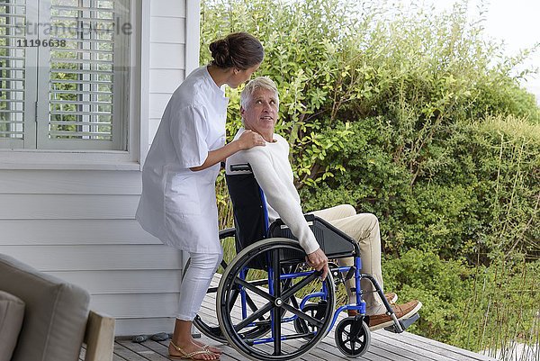 Krankenschwester als Assistentin eines älteren Mannes im Rollstuhl auf der Veranda