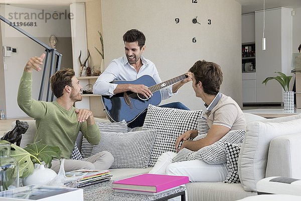 Glücklicher Mann spielt Gitarre mit seinen Freunden in seiner Nähe.