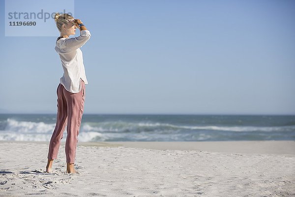 Schöne junge Frau am sonnigen Strand stehend