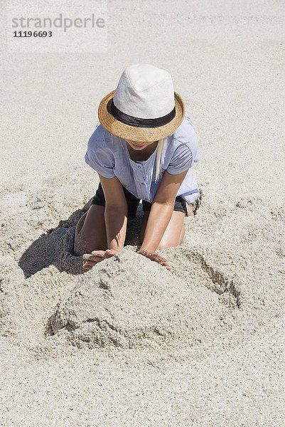 Hochwinkelansicht eines Mädchens  das eine Sandburg am Strand baut.