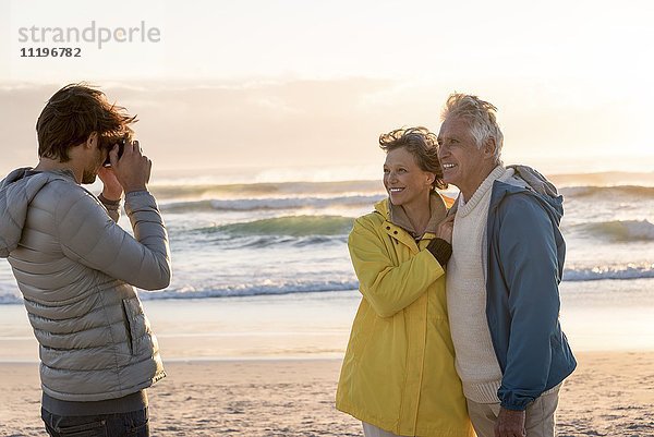 Junger Mann beim Fotografieren seiner Eltern mit Kamera am Strand