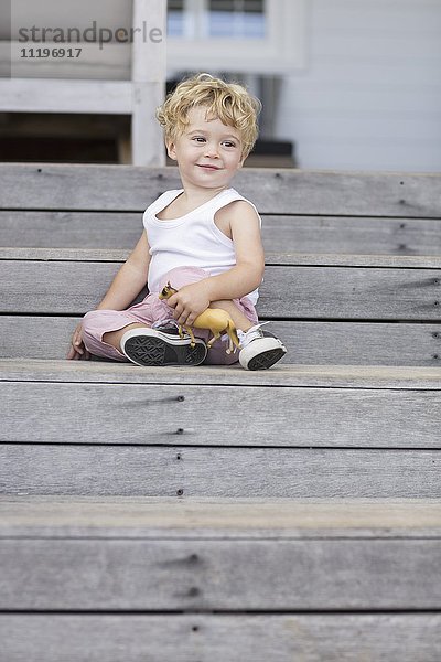 Süßer Junge sitzend auf einer Treppe mit Spielzeug