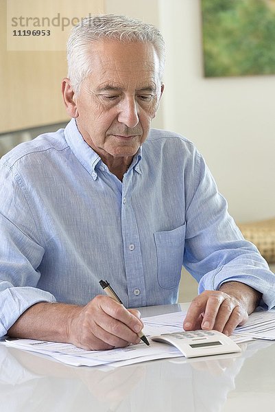 Älterer Mann  der einen Taschenrechner benutzt  während er zu Hause Papierkram erledigt.
