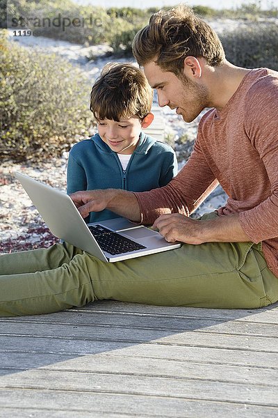 Vater und Sohn mit einem Laptop an der Strandpromenade