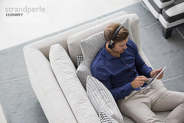 Junger Mann auf der Couch sitzend mit einem digitalen Tablett