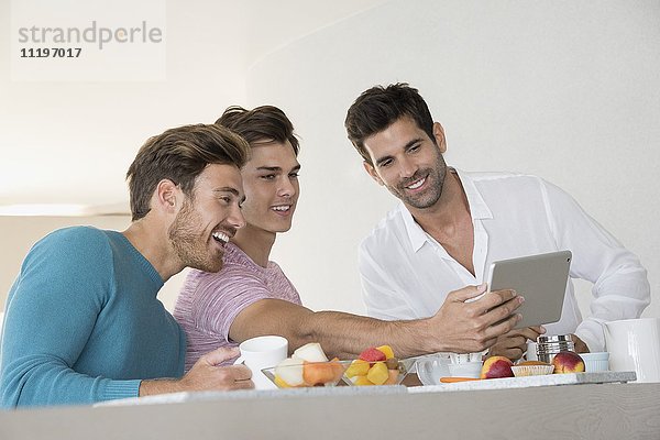 Glückliche männliche Freunde  die Selfie mit Tablette auf dem Frühstückstisch zu Hause einnehmen