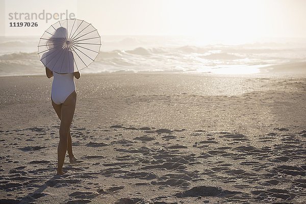 Rückansicht einer Frau mit Sonnenschirm am Strand