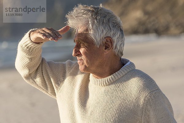 Älterer Mann beobachtet mit abschirmenden Augen am Strand