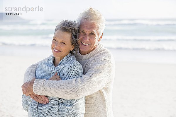 Alter Mann  der seine Frau von hinten am Strand umarmt.