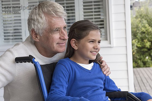 Glücklicher älterer Mann mit seiner Enkelin im Rollstuhl auf der Veranda