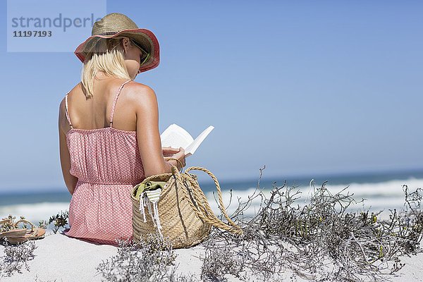 Schöne Frau  die ein Buch am Strand liest.