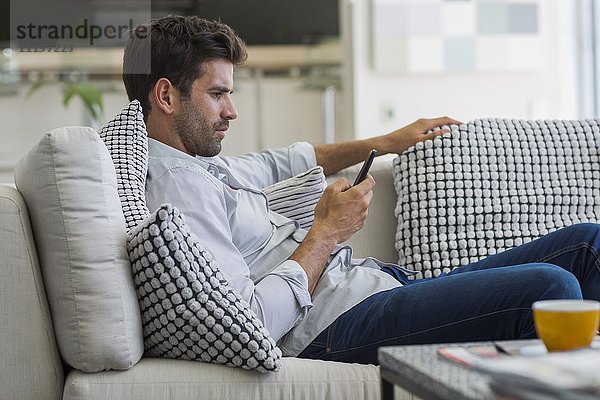 Mann  der auf einer Couch sitzt und ein Smartphone benutzt.