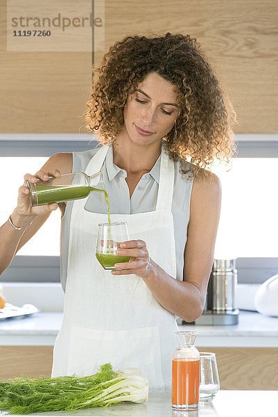 Frau gießt Gemüsesaft in ein Glas