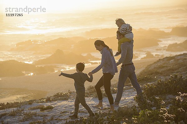 Glückliche junge Familie  die bei Sonnenuntergang am Strand spazieren geht.