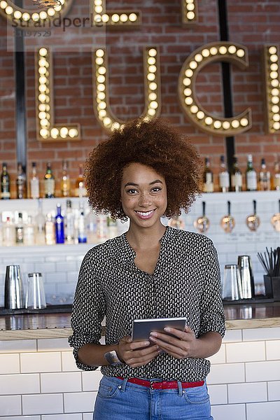 Porträt einer glücklichen jungen Frau mit einem digitalen Tablett an der Theke