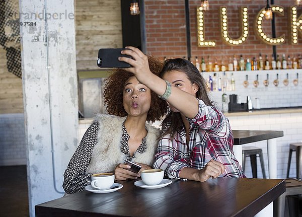 Weibliche Freunde  die einen Selfie mit Fotohandy im Cafe mitnehmen
