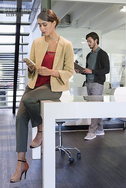 Geschäftsfrau mit einem Smartphone im Büro mit ihrem Kollegen im Hintergrund
