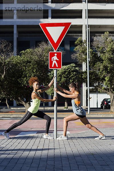 Junge Athletinnen beim Stretching an der Stange auf der Straße