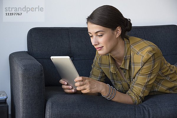 Junge schöne Frau mit einem digitalen Tablett auf der Couch